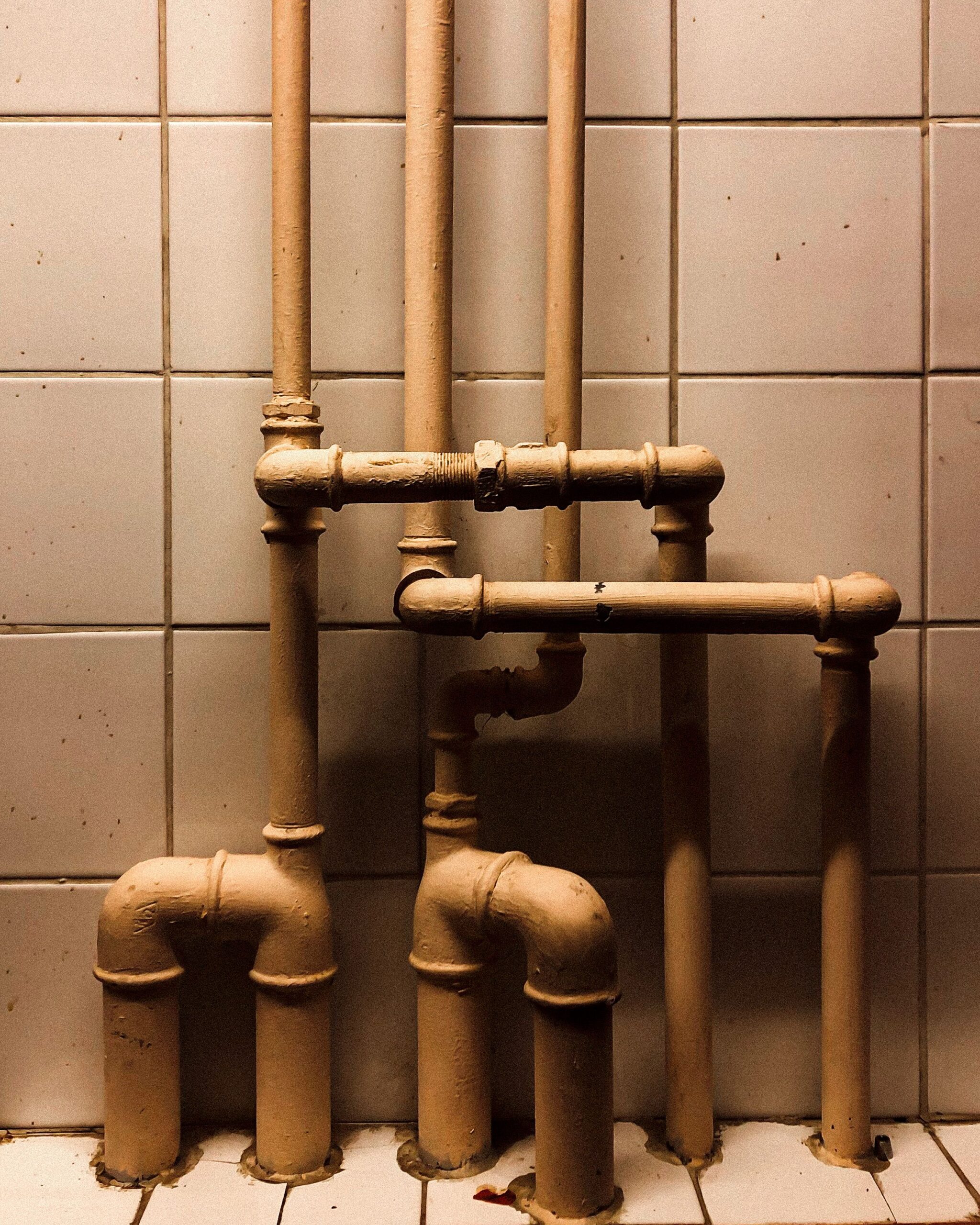 An artistic capture of vertical industrial pipes against a tiled wall, showcasing geometry.